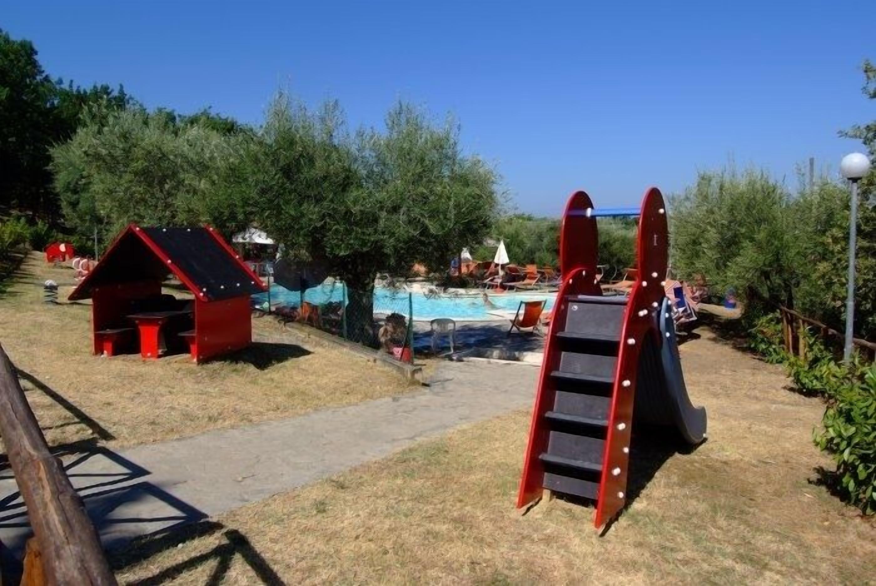 A playground with a slide and a small red playhouse.