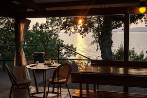 Una terraza con mesa y sillas, con vista a un cuerpo de agua al atardecer.