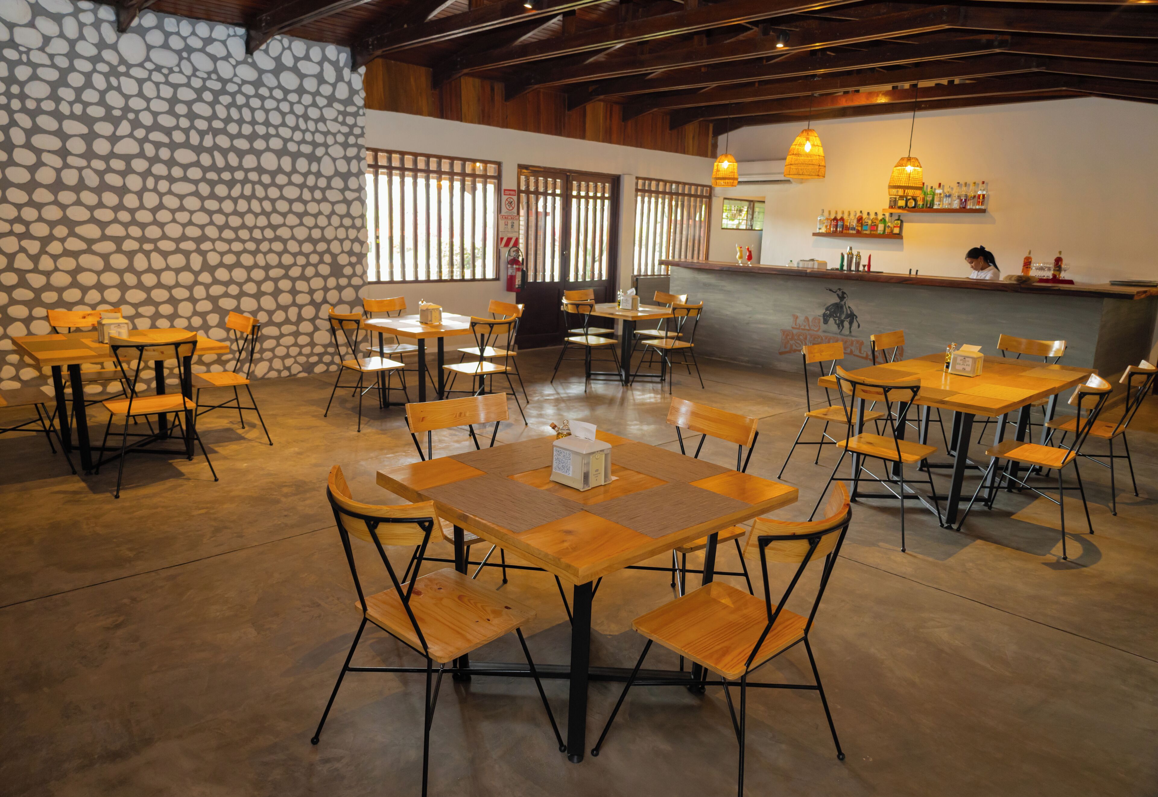 A spacious restaurant with wooden tables and chairs, a stone wall, and a bar area.