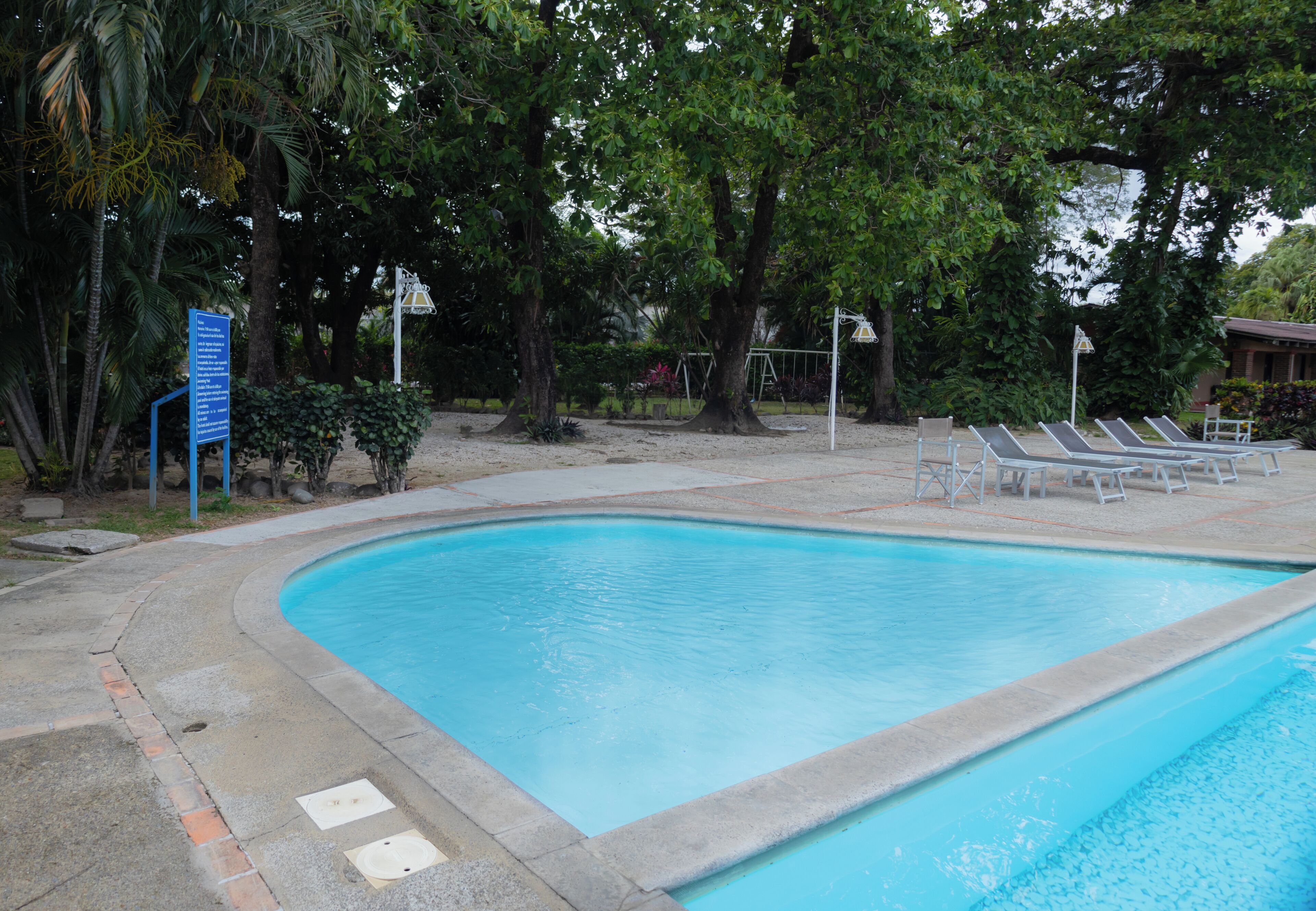A swimming pool with a concrete edge, surrounded by trees and a sandy area.