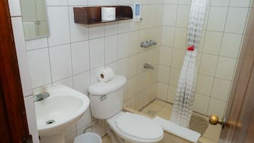 A bathroom with a sink, two toilets, a shower curtain, and a small trash bin.