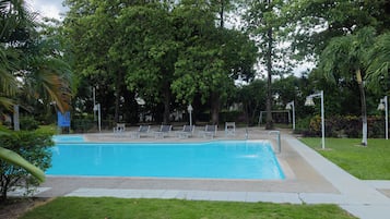 A rectangular swimming pool with a tiled deck, surrounded by grass and trees.