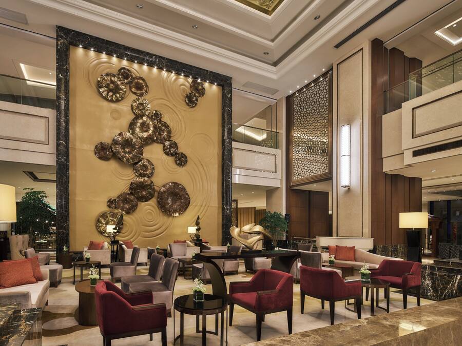 A spacious lobby with a large decorative wall, multiple seating areas, and a modern staircase.