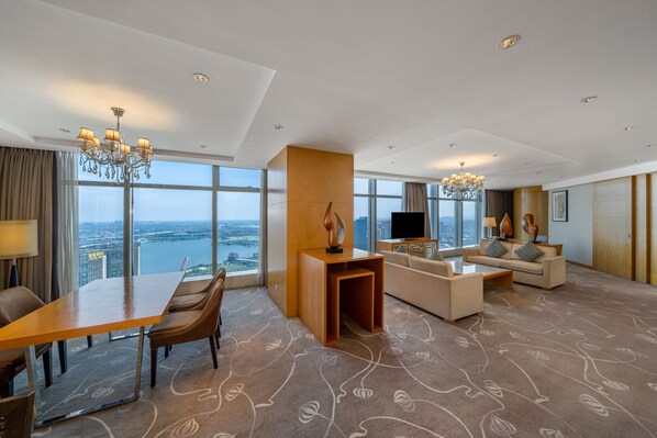 A modern hotel room with a dining area, a living room with a sofa and TV, large windows with a city view, and a chandelier. - Crowne Plaza Shaoxing by IHG (Shaoxing)