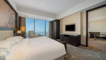 A hotel room with a large bed, a desk, a television, and a view of the city.