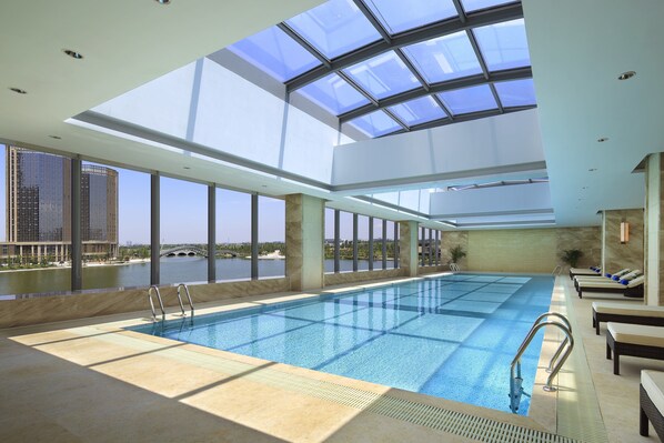 A large indoor swimming pool with clear views of a river and buildings, surrounded by sunlit areas with seating. - Crowne Plaza Shaoxing by IHG (Shaoxing)