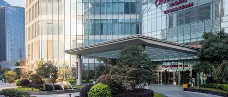 A modern hotel with a glass facade, a covered entrance, and landscaped gardens.