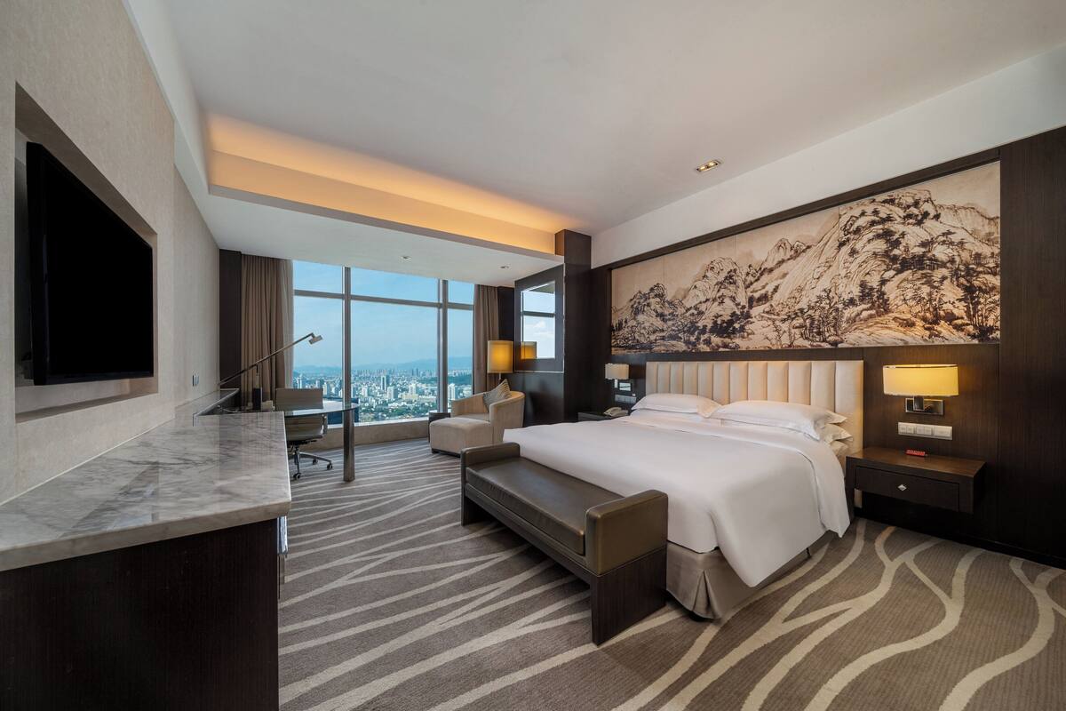 Quarto de hotel moderno com uma cama grande, uma escrivaninha e vista para a cidade.