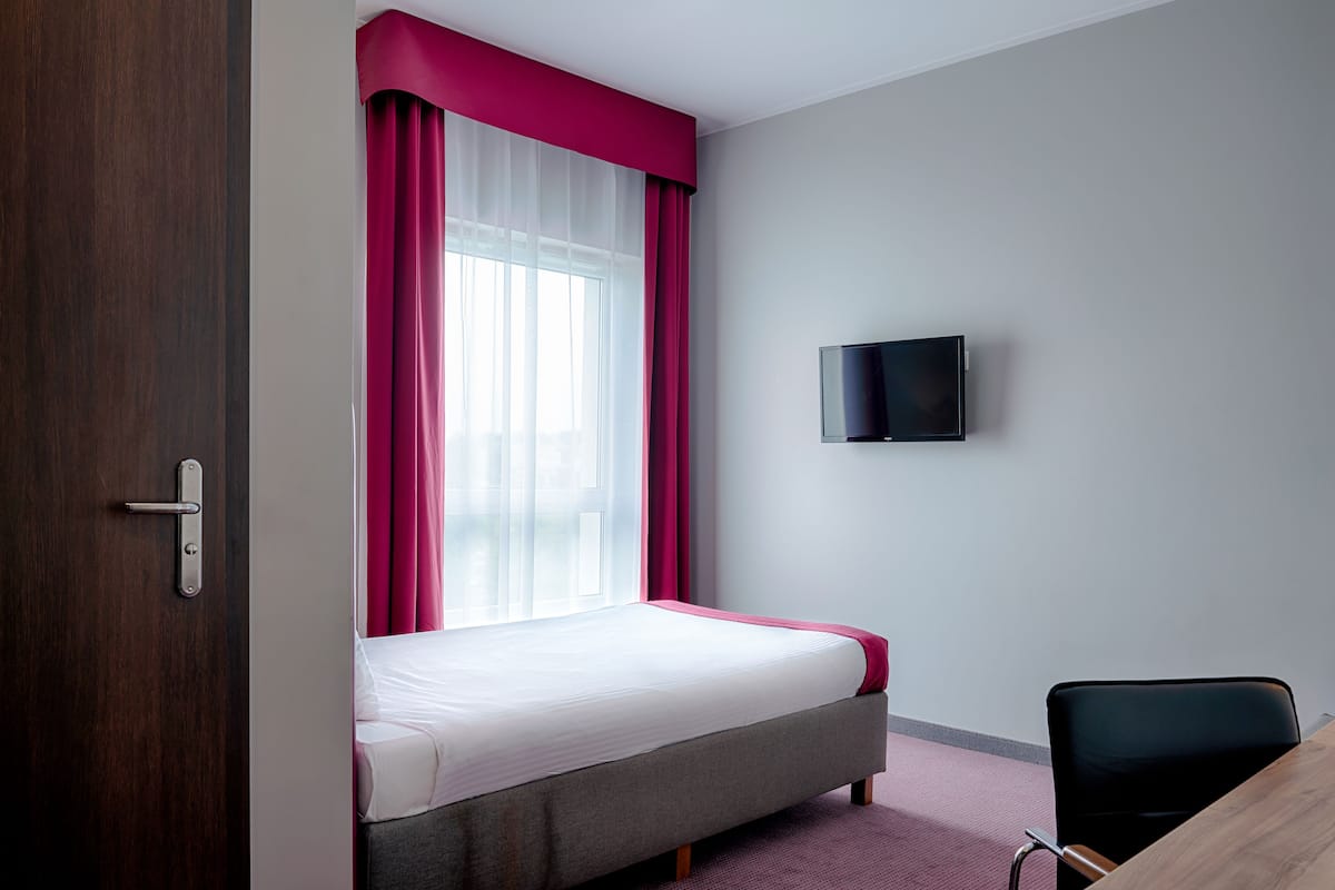 Une chambre d’hôtel avec un lit, un téléviseur fixé au mur et un bureau avec une chaise.
