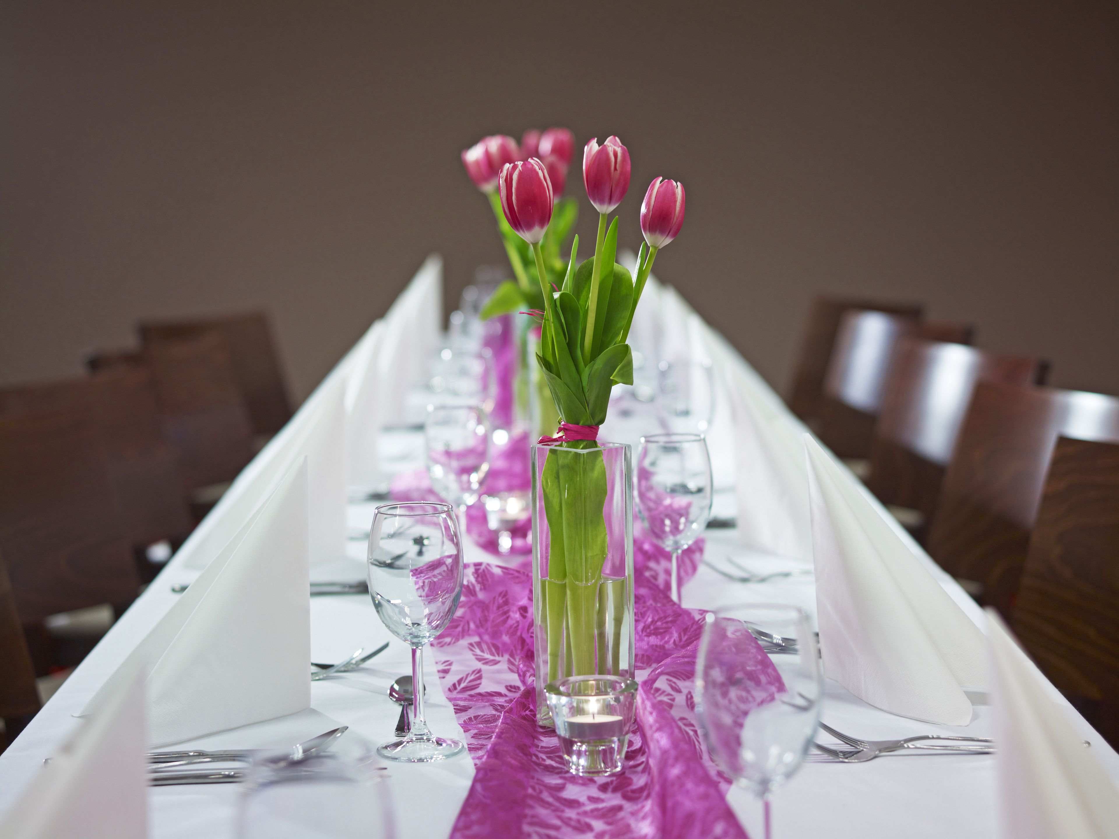 A table set with clear glassware, pink tulips, and a purple table runner.