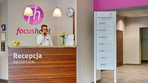 A reception desk with a wooden finish and a sign listing conference room names. - Focus Hotel Katowice Chorzow (Chorzow)