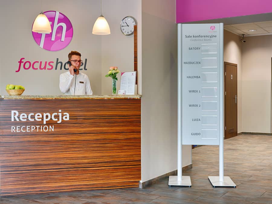 Taulell de recepció amb acabat de fusta i un cartell amb els noms de les sales de conferències.