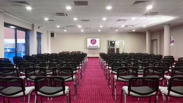 A conference room with rows of chairs, a projector screen, and a carpeted floor.