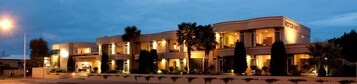 Um hotel com vários andares e fachada curva, janelas iluminadas e uma placa com a inscrição "MOTOR INN".