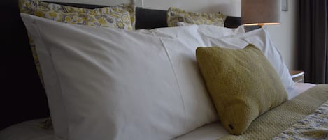 A neatly made bed with white and patterned bedding, a lamp, and a wall-mounted light fixture.