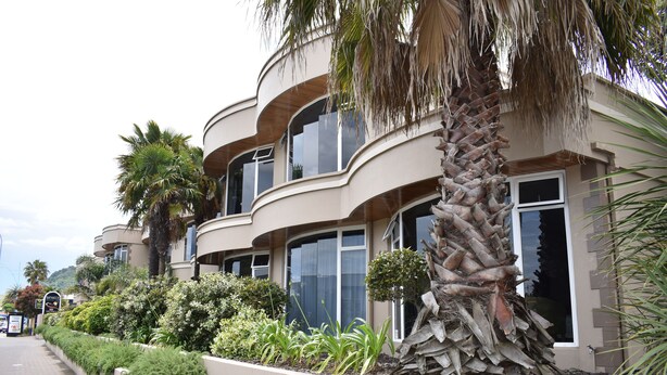 Un edificio de varios pisos con balcones curvos, palmeras y un jardín ajardinado.