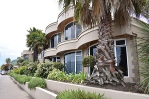 A multi-story building with curved balconies, palm trees, and a landscaped garden. - Baywatch Motor Inn (Tauranga)