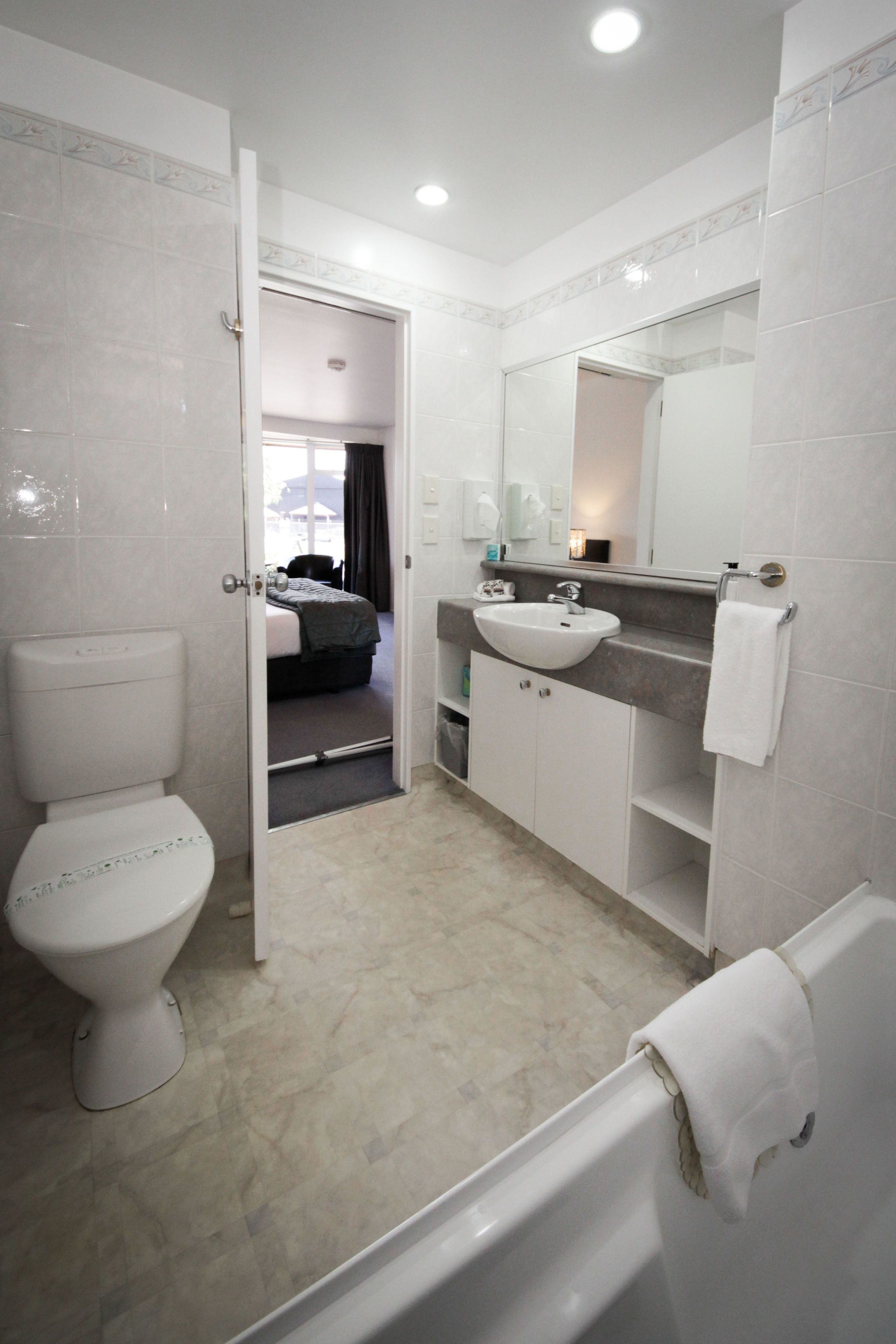 Et moderne badeværelse med toilet, vask og badekar. Et spejl og et håndklædestativ er synlige.