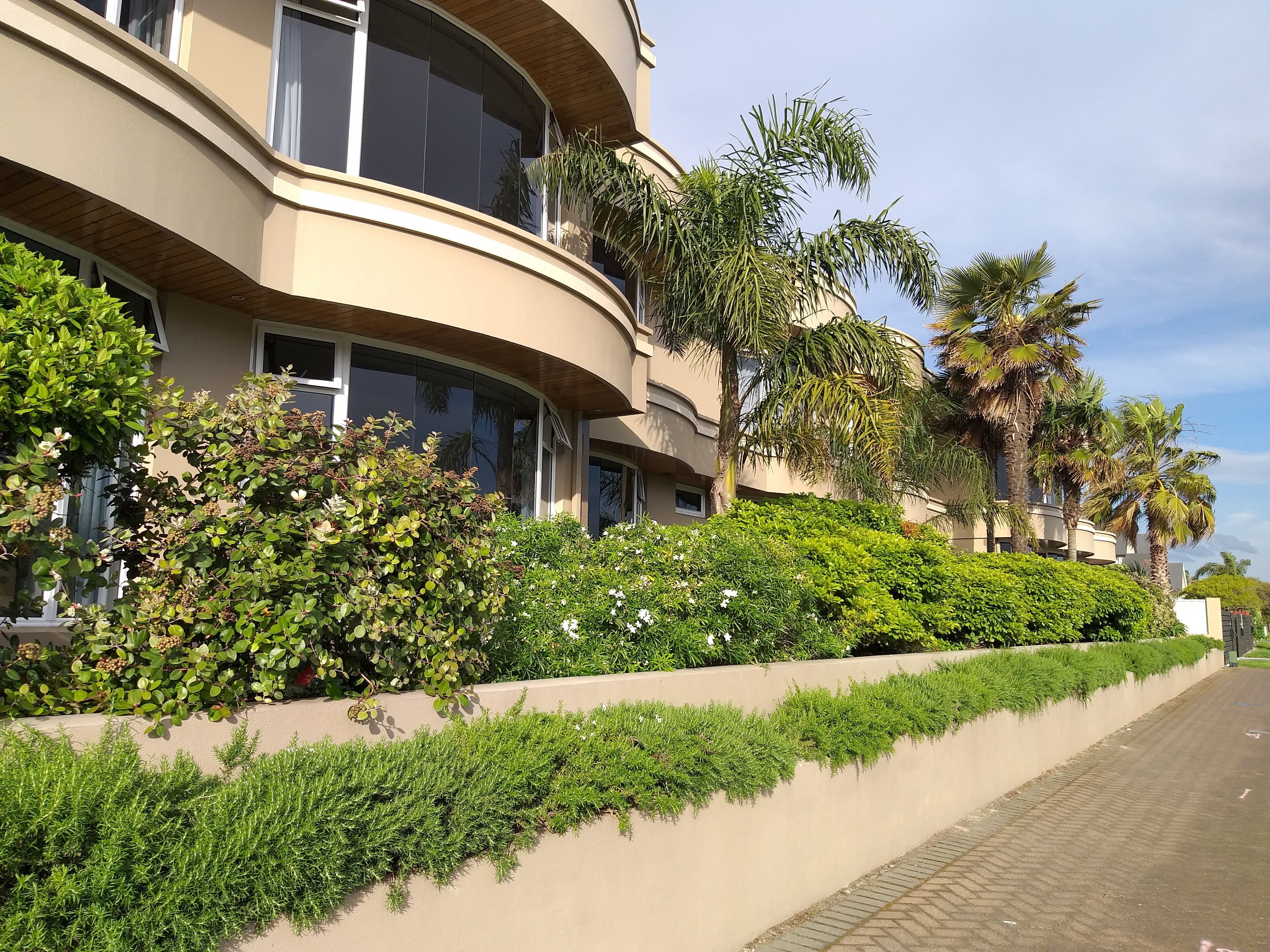 Un edificio moderno con balcones curvos, abundante vegetación y palmeras.
