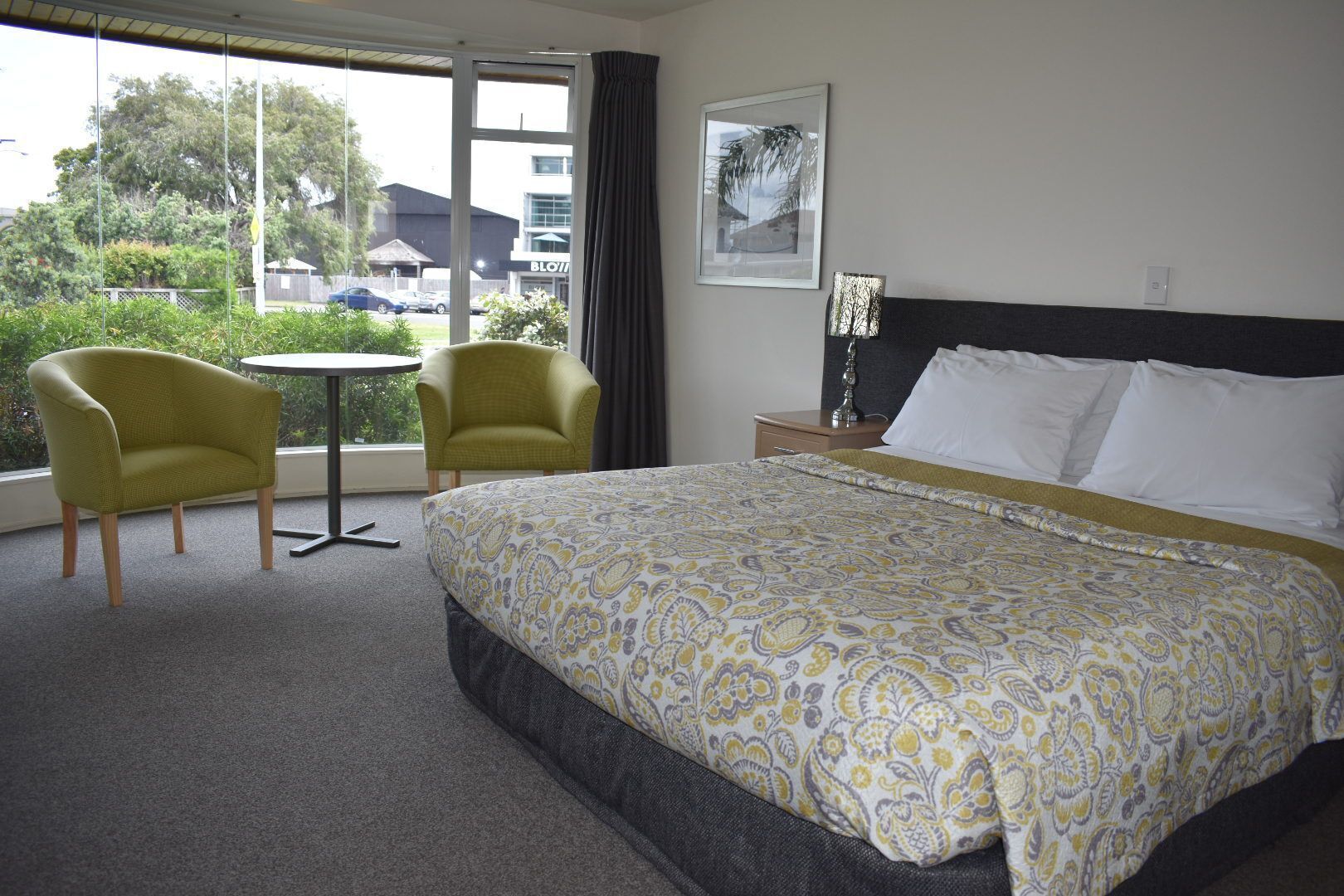 A hotel room with a large bed, two armchairs, a small table, and a window with a view of the outside.