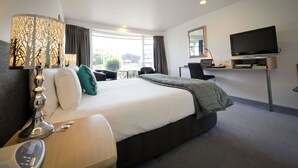 Habitación de hotel con una cama grande, un escritorio con televisor, una lámpara y vistas al exterior.