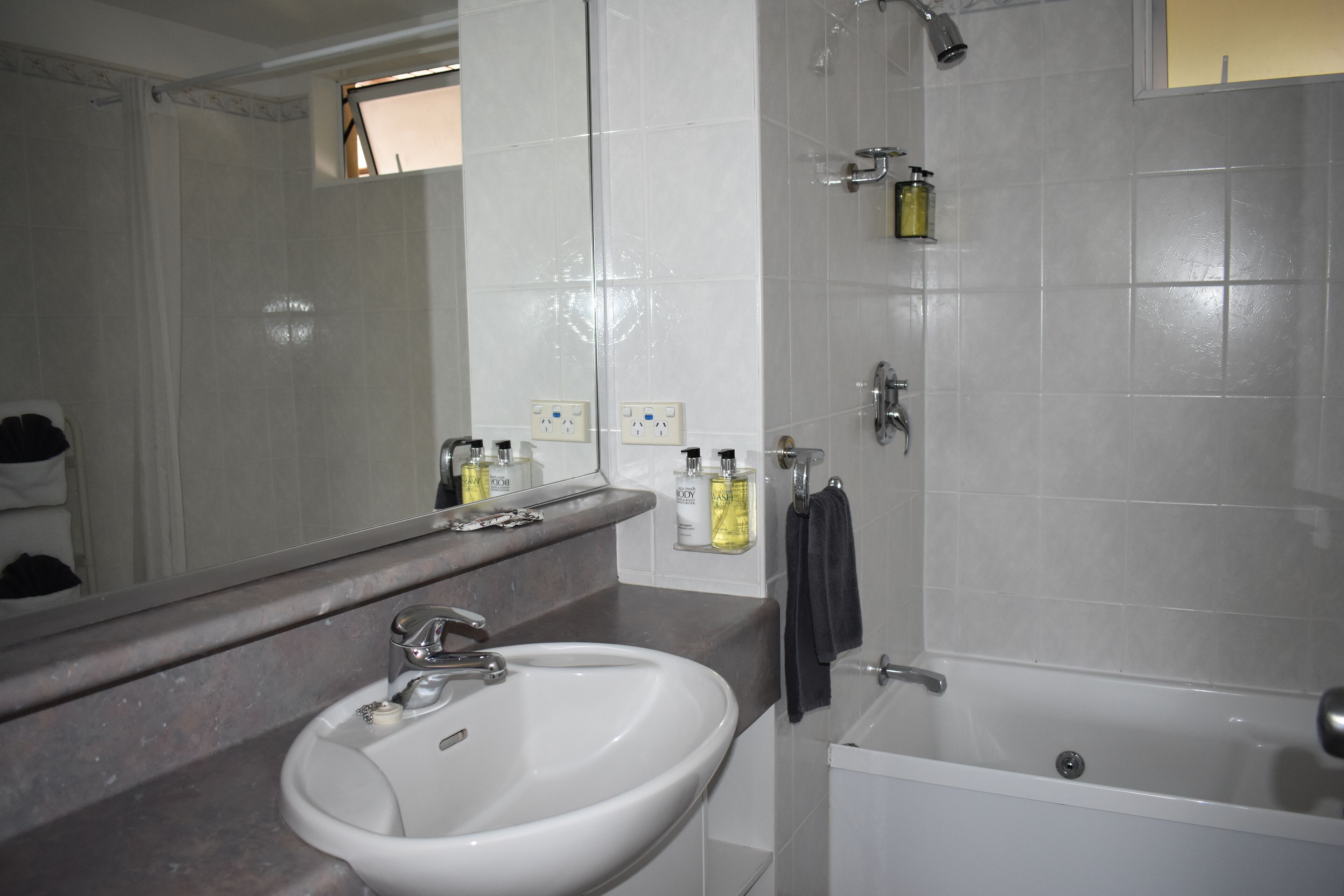 A bathroom with a white sink, mirror, and bathtub. There are toiletries on the counter.