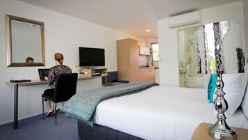 A hotel room with a bed, a desk with a computer, a television, and a bathroom visible through an open door.