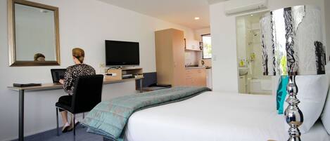 A hotel room with a bed, a desk with a computer, a television, and a bathroom visible through an open door.