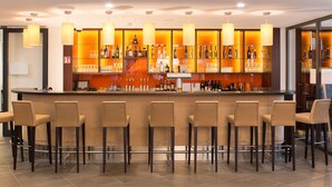 Zona de bar con varios taburetes, una barra con botellas y vasos, e iluminación colgante.