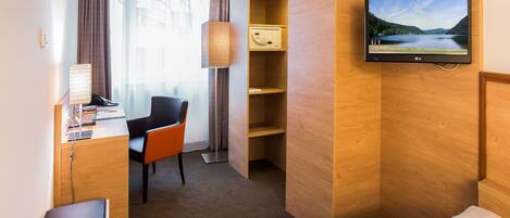 A hotel room with a desk, chair, TV, and a bed.