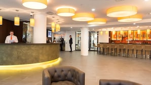 Un vestíbulo de hotel con mostrador de recepción, zona de bar y asientos.