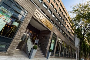 Et moderne hotel med murstensfacade, store vinduer og et skilt, der angiver, at der serveres morgenmad.