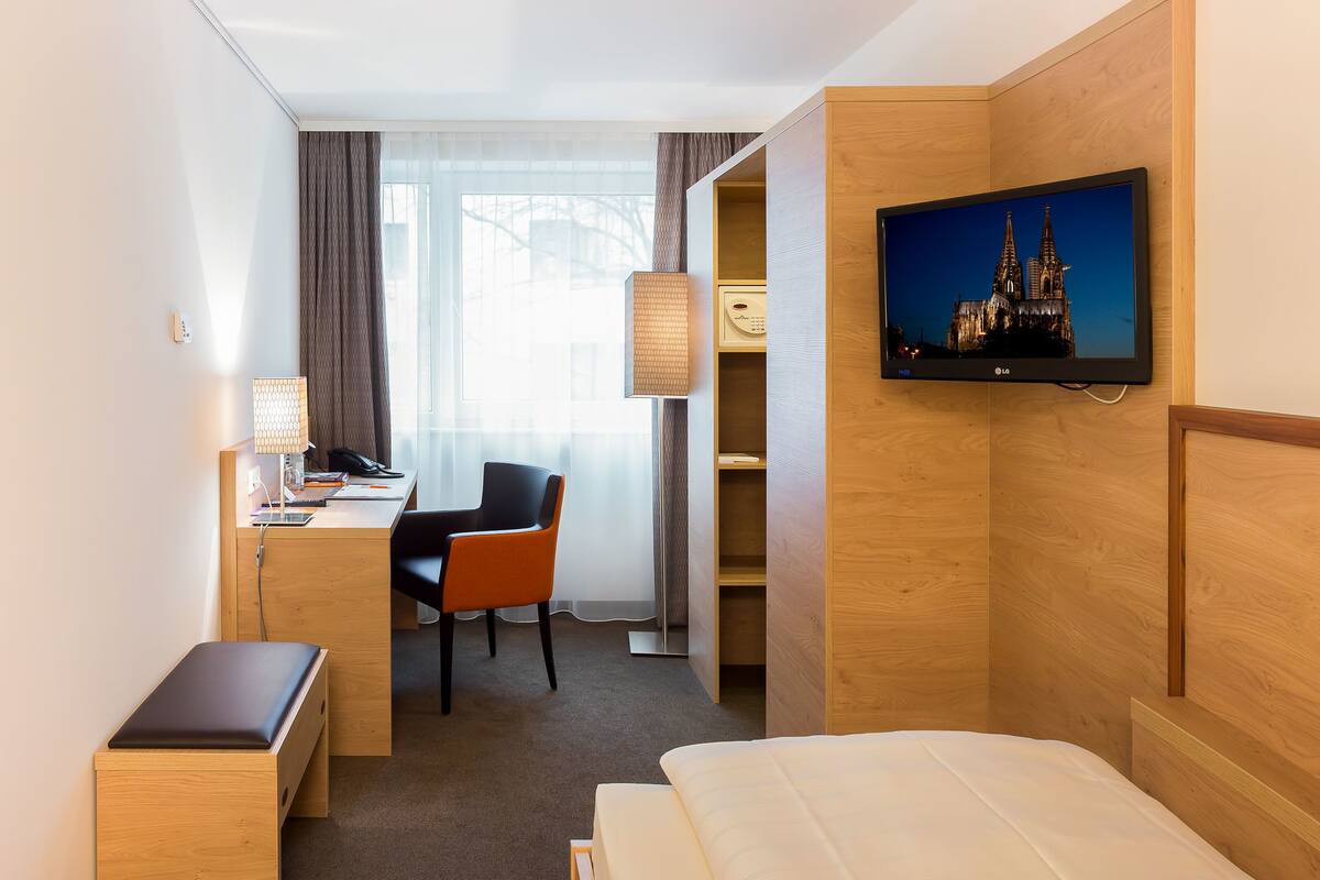 Ein Hotelzimmer mit Bett, Schreibtisch, Stuhl, Fernseher und Kleiderschrank.
