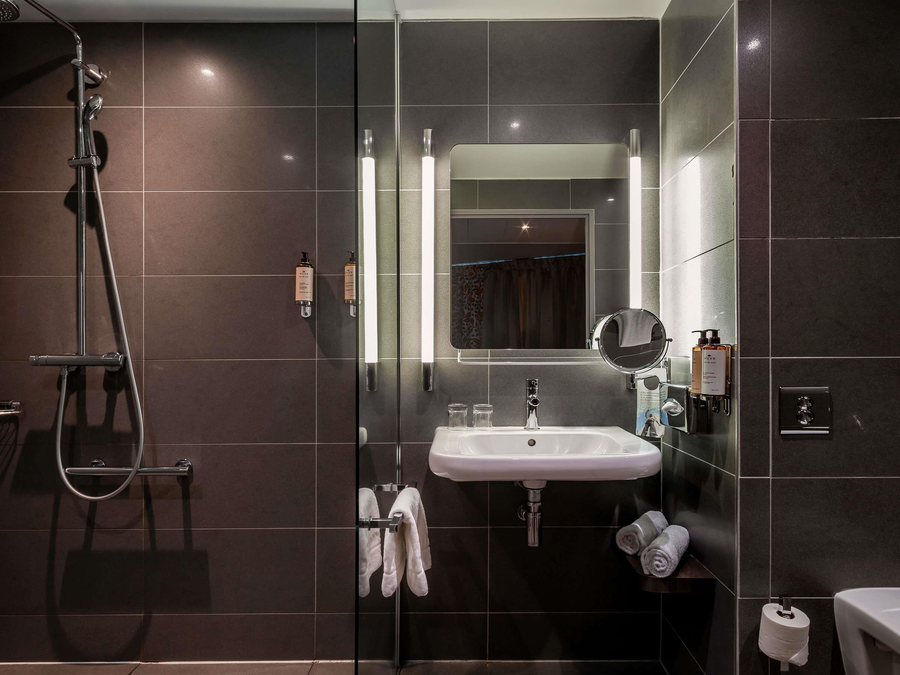 A modern bathroom with a glass-enclosed shower, a white sink, and a large mirror.