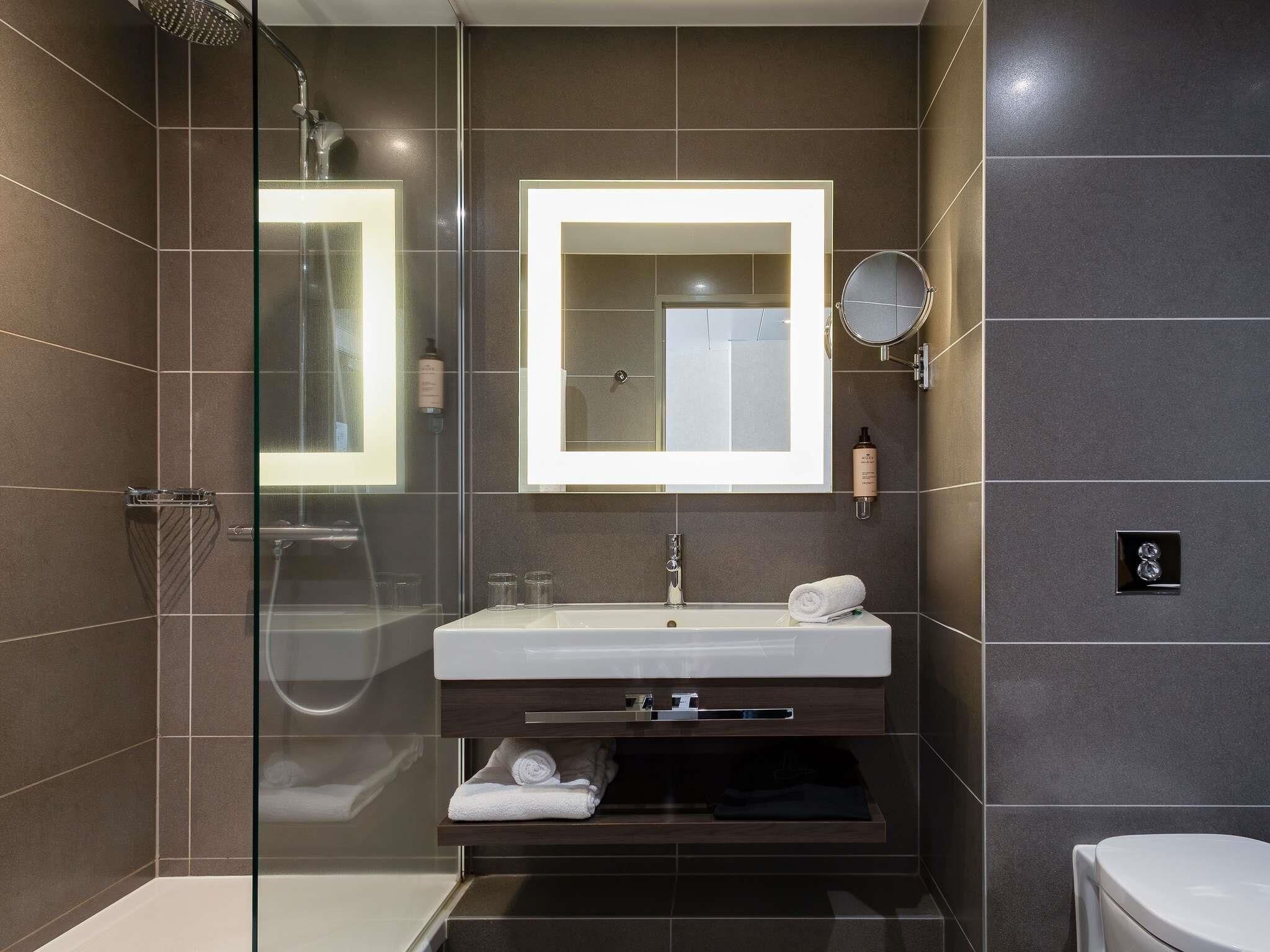 Un baño moderno con ducha de vidrio, un lavabo blanco con un espejo encima y un inodoro.