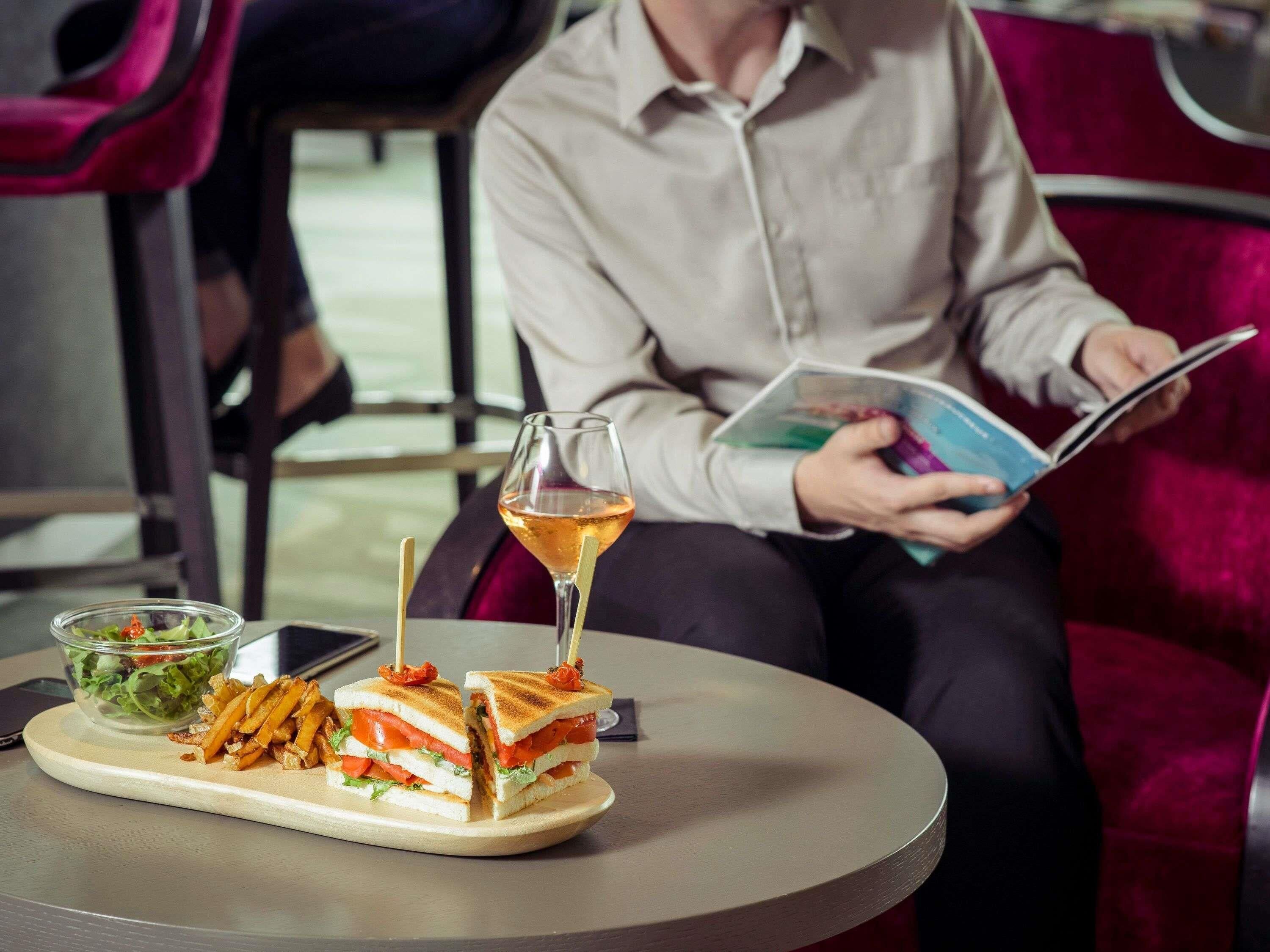 Una persona seduta a tavola con un panino, un bicchiere di vino e un'insalata.