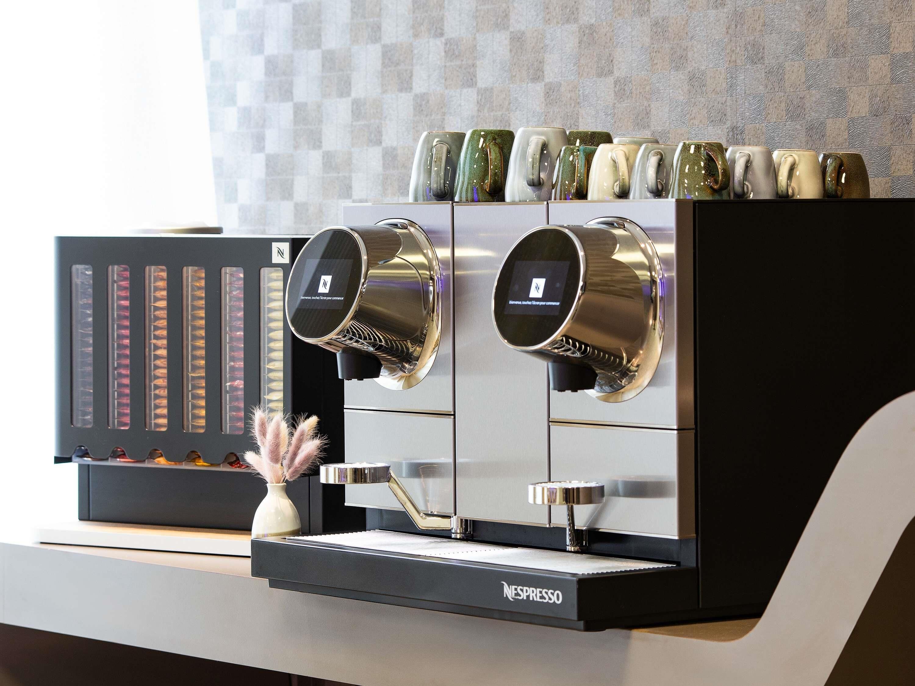 A Nespresso coffee machine with a digital interface, a selection of mugs, and a decorative vase with feathers.
