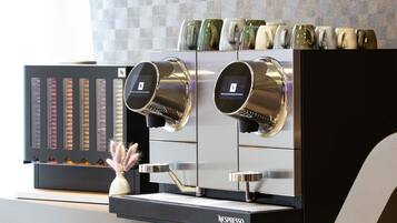 A Nespresso coffee machine with a digital interface, a selection of mugs, and a decorative vase with feathers.