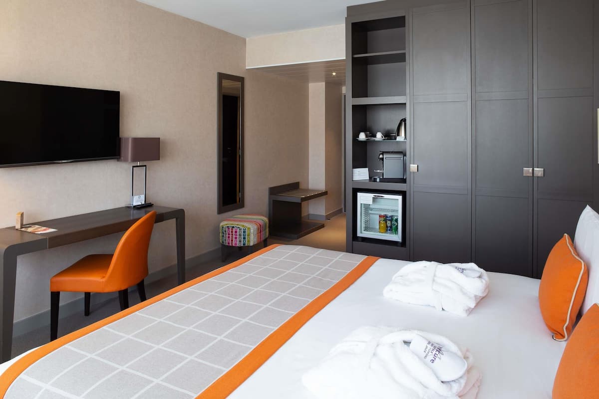 Habitación de hotel con cama, escritorio, silla, televisor, armario y mini refrigerador.