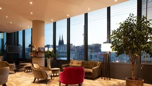 Un moderno vestíbulo de hotel con ventanas amplias, un televisor de pantalla plana y diversas opciones de asientos.
