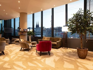 A modern hotel lobby with large windows, a flat-screen TV, and a variety of seating options. - Mercure Clermont Ferrand Centre Jaude (Clermont-Ferrand)