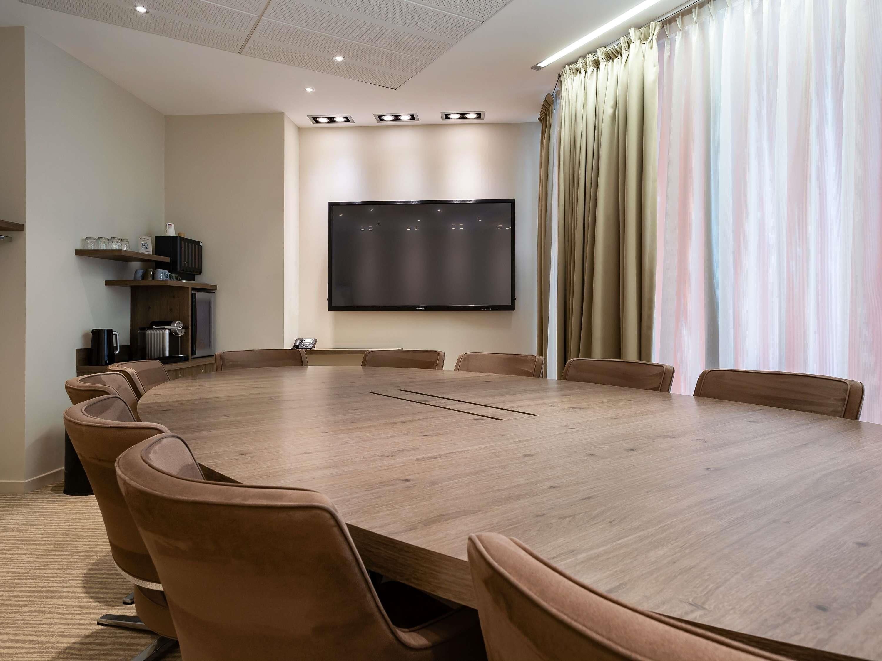 A conference room with a large table, chairs, a flat-screen TV, and a coffee machine.
