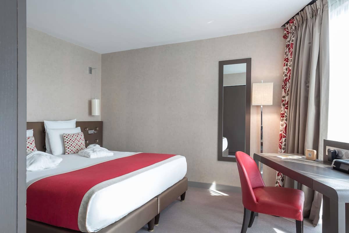 Una habitación de hotel con cama, escritorio, silla, espejo y lámpara.