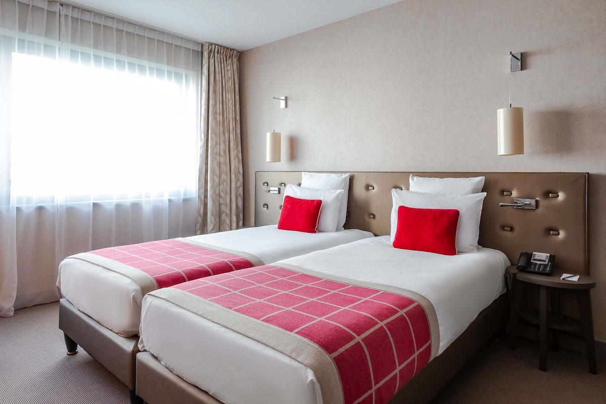 Habitación de hotel con dos camas, una mesita de noche, un teléfono y una ventana con cortinas.
