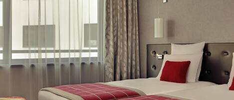 Une chambre d’hôtel avec deux lits, une table de chevet, une lampe et une fenêtre avec des rideaux.