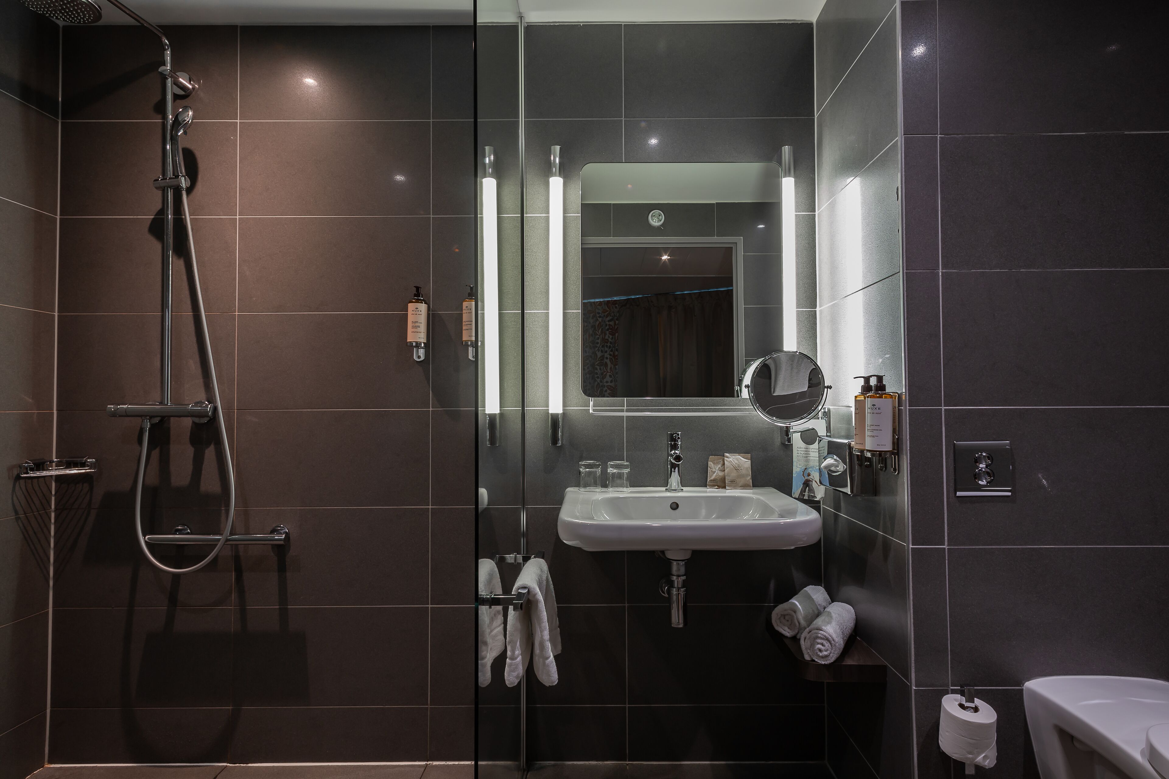 Een moderne badkamer met een douchecabine van glas, een wastafel en een spiegel.