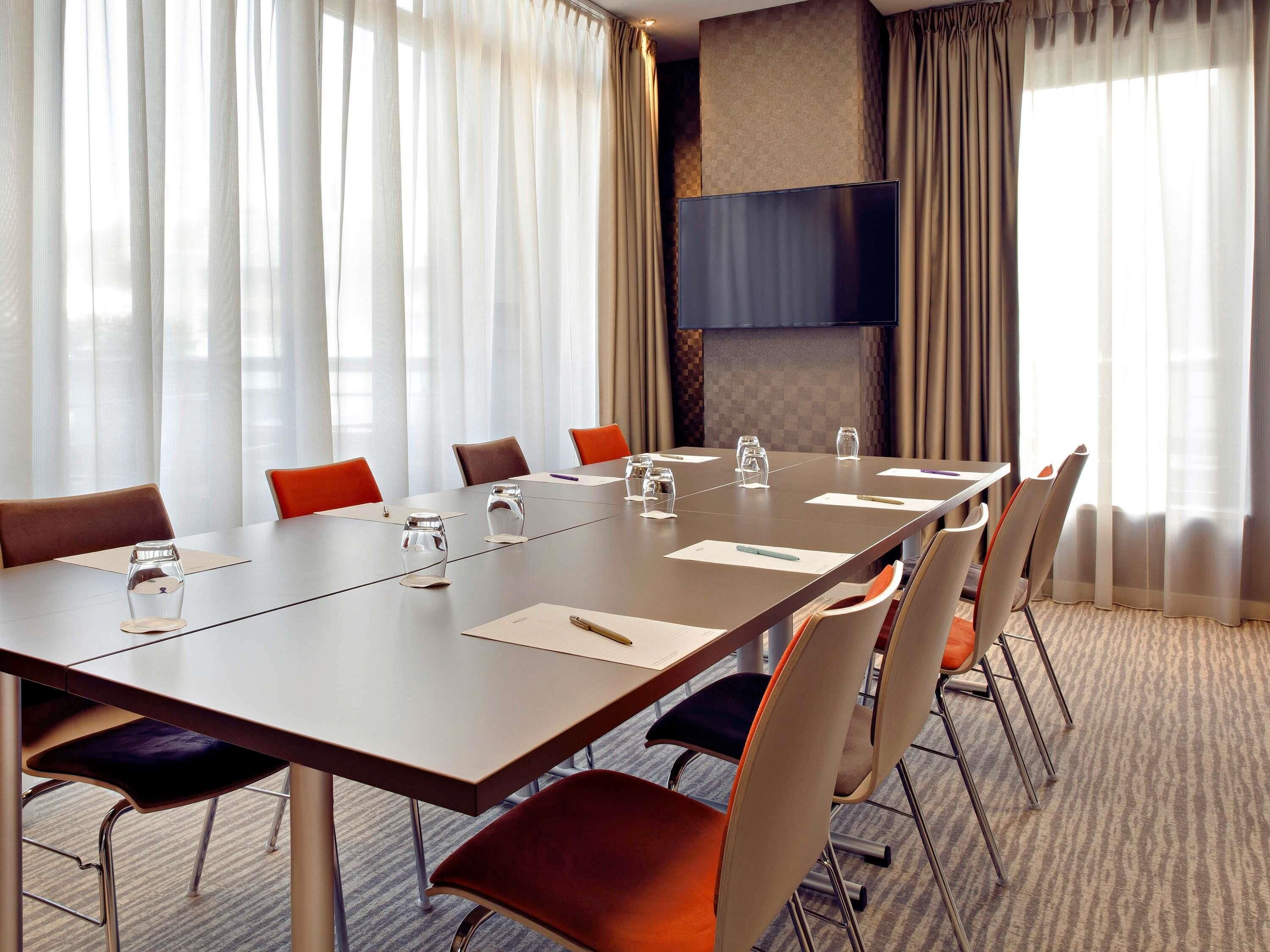A conference room with a long table, chairs, and a television screen.