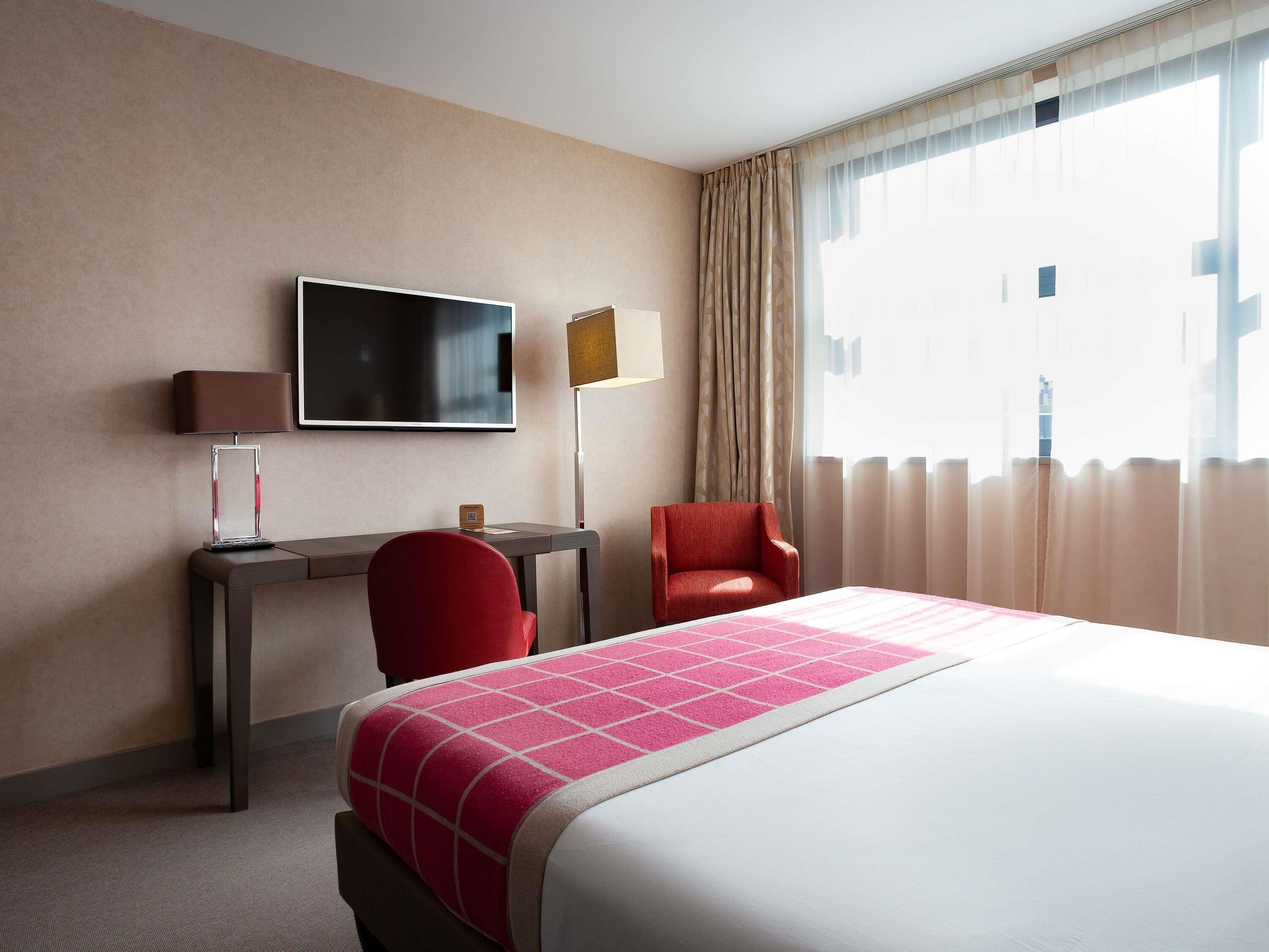 A hotel room with a bed, a desk, a chair, a TV, and a window with curtains.