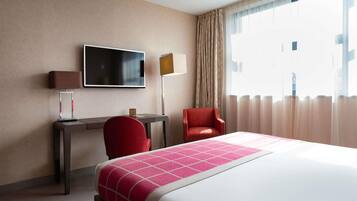 A hotel room with a bed, a desk, a chair, a TV, and a window with curtains.