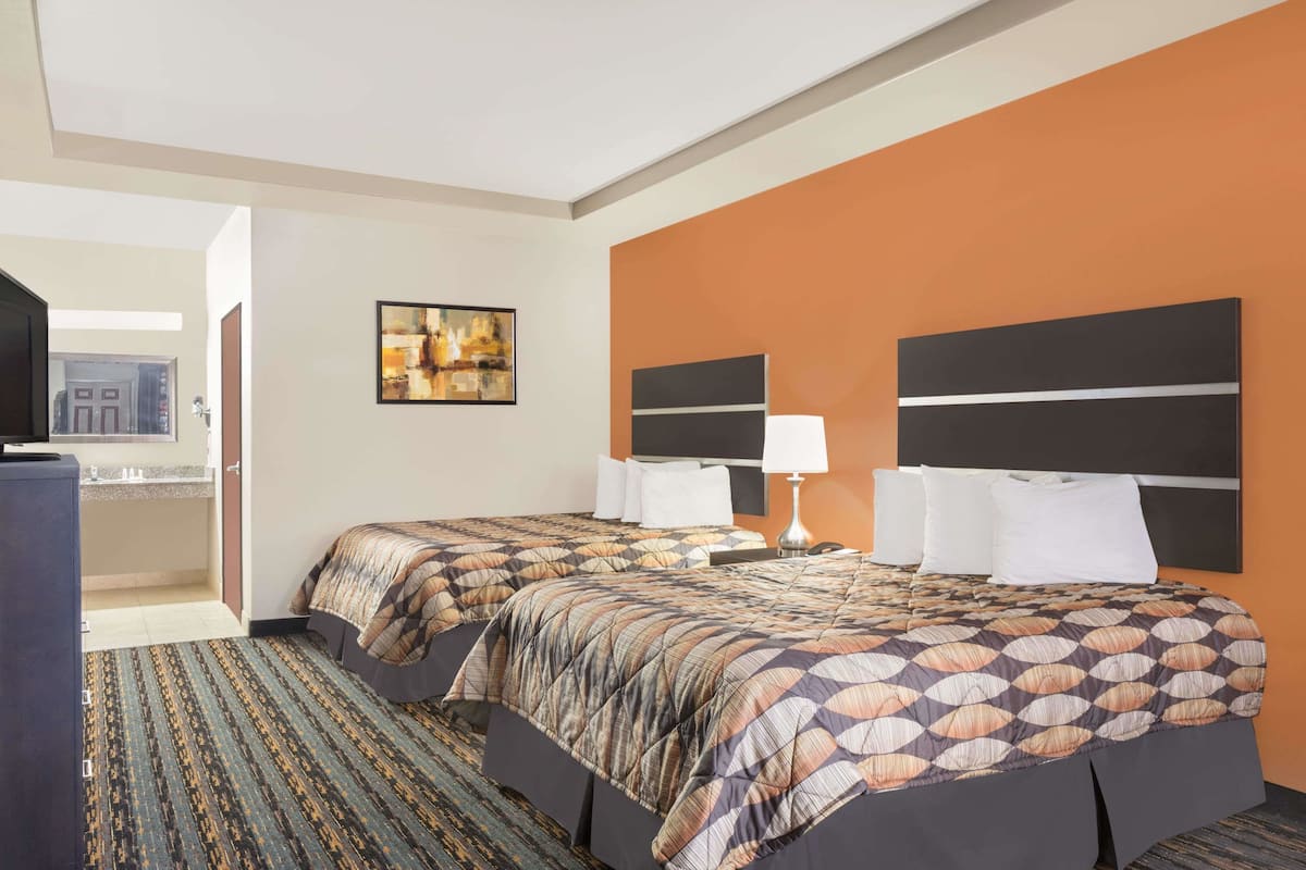A hotel room with two beds, a TV, a painting on the wall, and a bathroom visible through an open door.